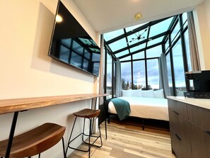 A modern room with a bed, a TV, a wooden desk, and a window with a view.
