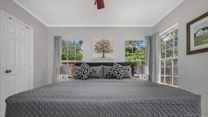 A bedroom with a large bed, two windows, and a view of greenery outside. - The private home features two master suites with King beds and full attached bathrooms. The loft is 3rd private getaway with a Queen bed and attached full bath. Fully stocked kitchen and a separate Oak dining area. (Dallas)