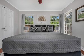 A bedroom with a large bed, two windows, and a view of greenery outside.