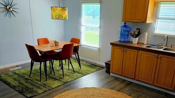 Une cuisine moderne avec des meubles en bois, une table à manger avec des chaises et un grand distributeur d’eau.