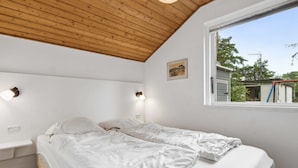 Een slaapkamer met twee bedden, houten balken in het plafond, een raam met uitzicht en wandlampen.