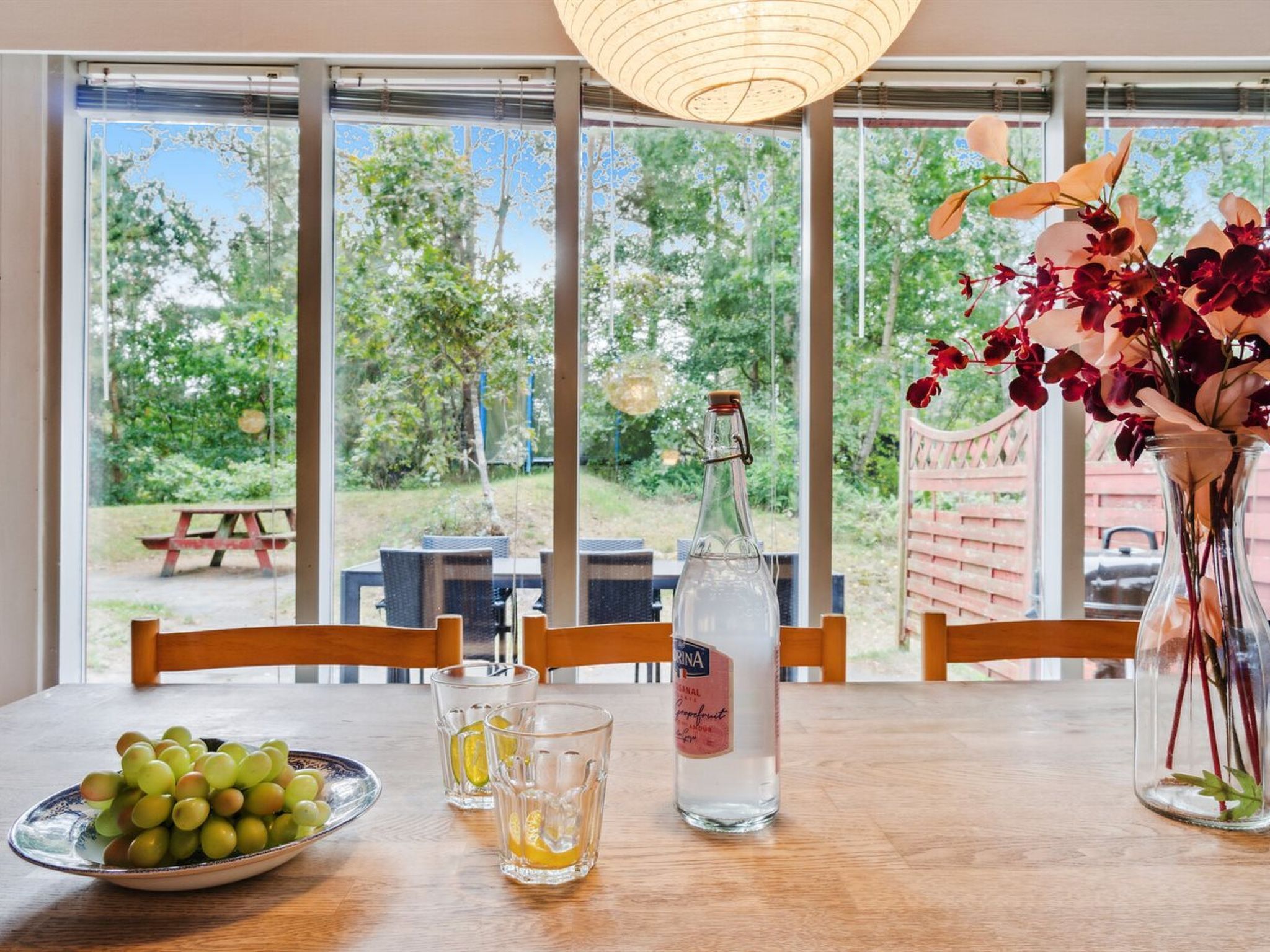 Ein Esstisch mit einer Wasserflasche, einer Platte Trauben und einer Vase mit Blumen.