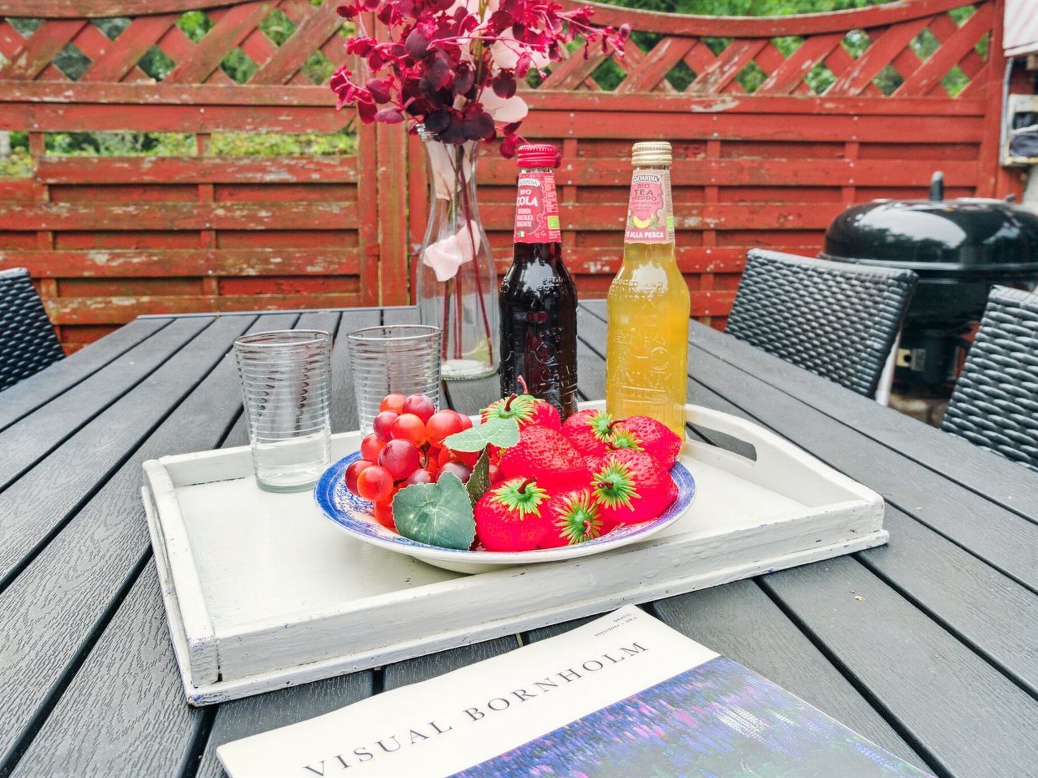 A tray with a plate of strawberries and grapes, two bottles, and a book titled "Visual BORNHOLM" on a wooden table.