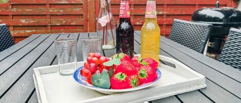 A tray with a plate of strawberries and grapes, two bottles, and a book titled "Visual BORNHOLM" on a wooden table.