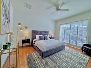A bedroom with a bed, bedside tables, a floor lamp, a ceiling fan, and a large window.