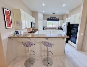 A modern kitchen with white cabinets, granite countertops, a built-in oven, and a window with a view. - 5 Star-Rated Indian Wells 5 Bedroom, Mtn View, Cas (Indian Wells)