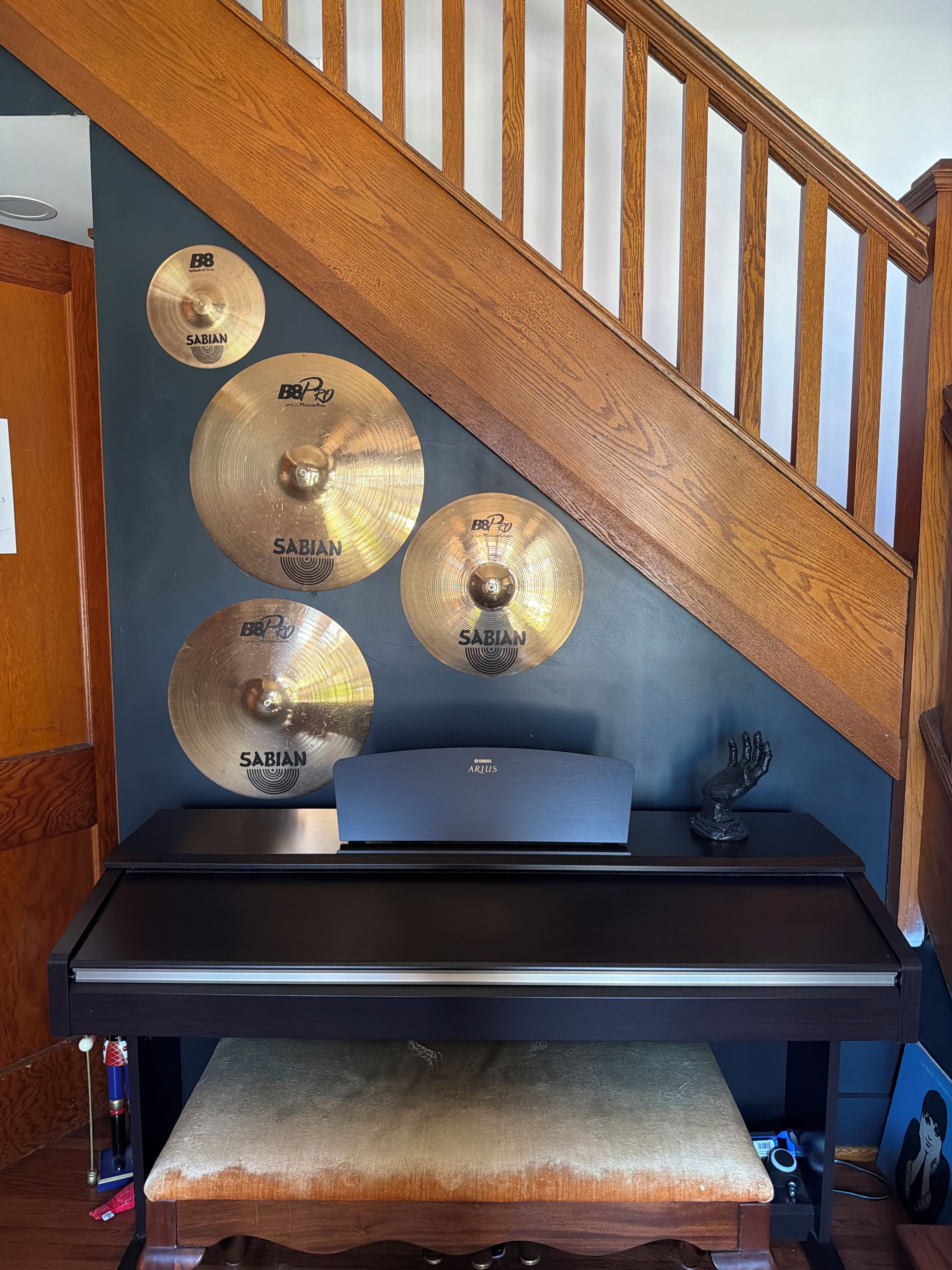 A room with a wooden staircase, a black desk, and multiple Sabian brand cymbals mounted on the wall.