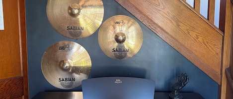 A room with a wooden staircase, a black desk, and multiple Sabian brand cymbals mounted on the wall.