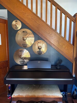 Une pièce avec un escalier en bois, un bureau noir et plusieurs cymbales de la marque Sabian fixées au mur.