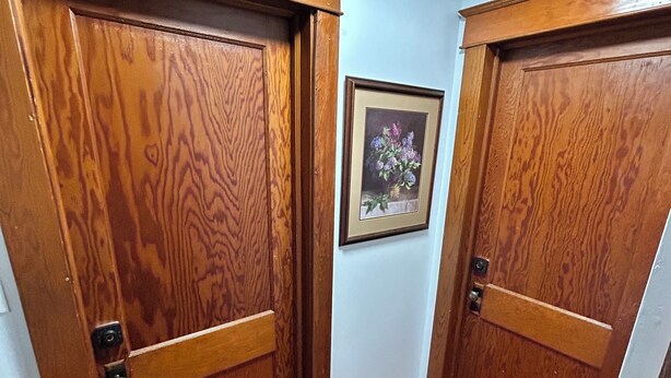Un couloir avec une porte double en bois et un tableau encadré accroché au mur.