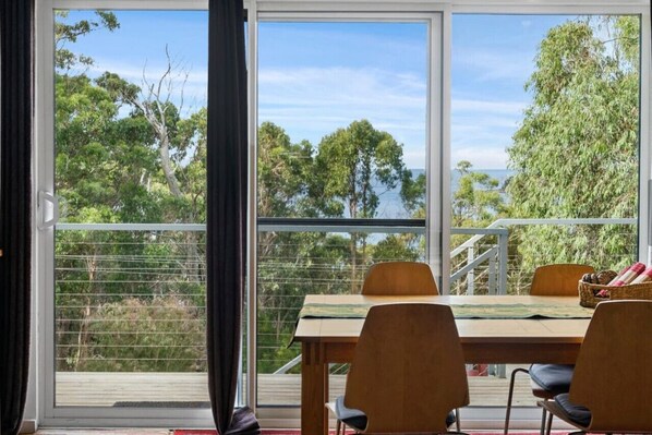 A dining area with a table and chairs, large windows with a view of trees and a body of water.