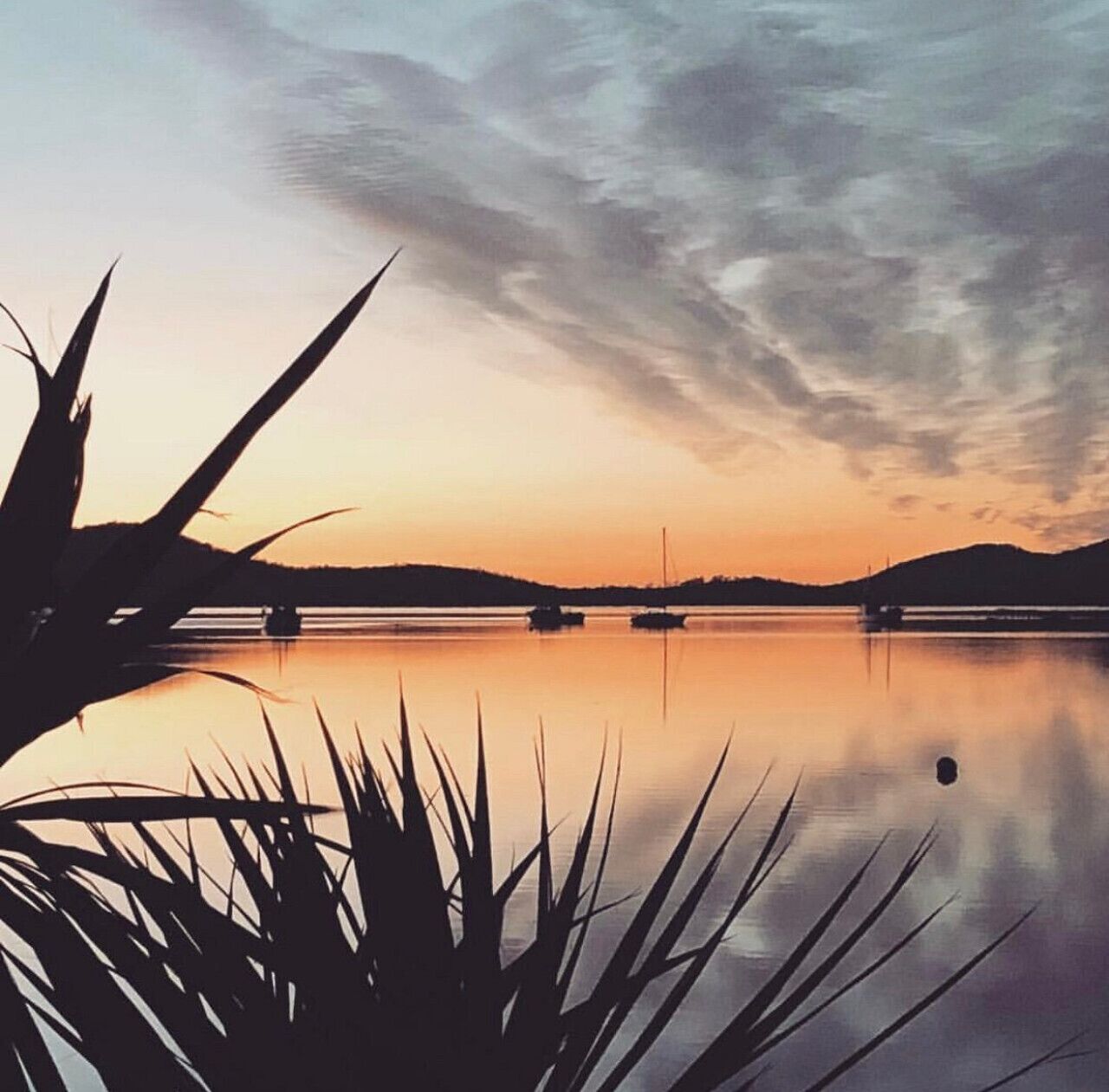 A calm lake at sunset with boats, surrounded by hills and sparse vegetation.