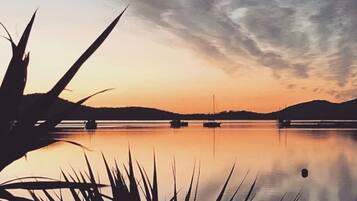A calm lake at sunset with boats, surrounded by hills and sparse vegetation.