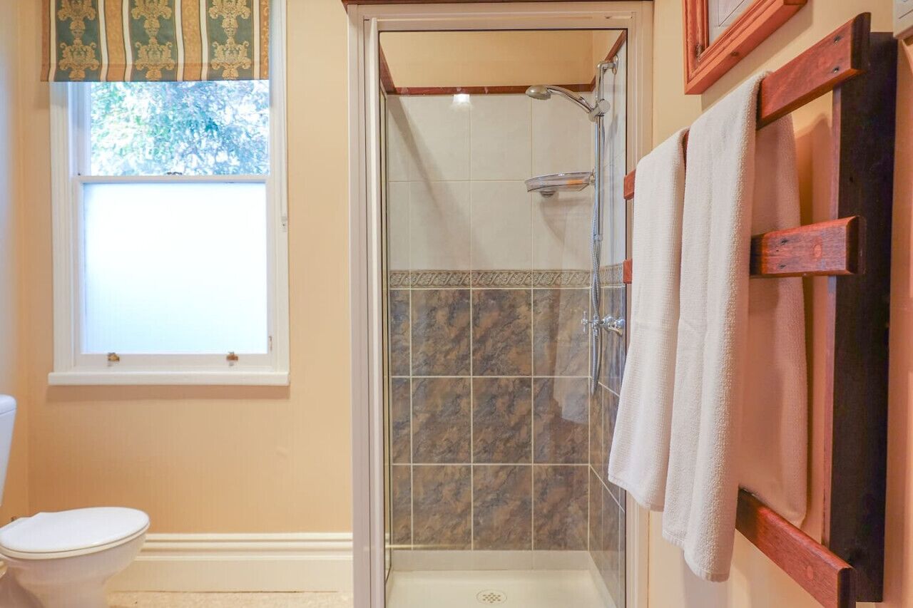 Une salle de bain avec une douche à parois de verre, des toilettes et une fenêtre avec des rideaux.
