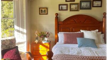 A bedroom with a wooden bed, a nightstand, a chair, and a window with a view of greenery.