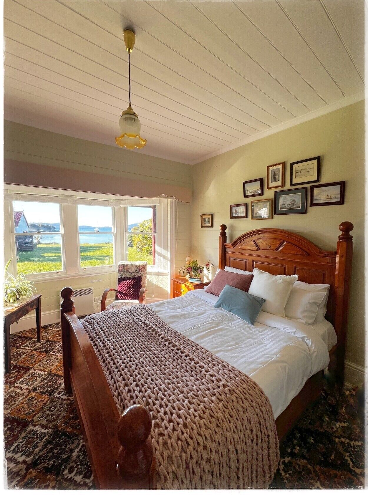 A bedroom with a large bed, a wooden headboard, a window with a view, and framed pictures on the wall.