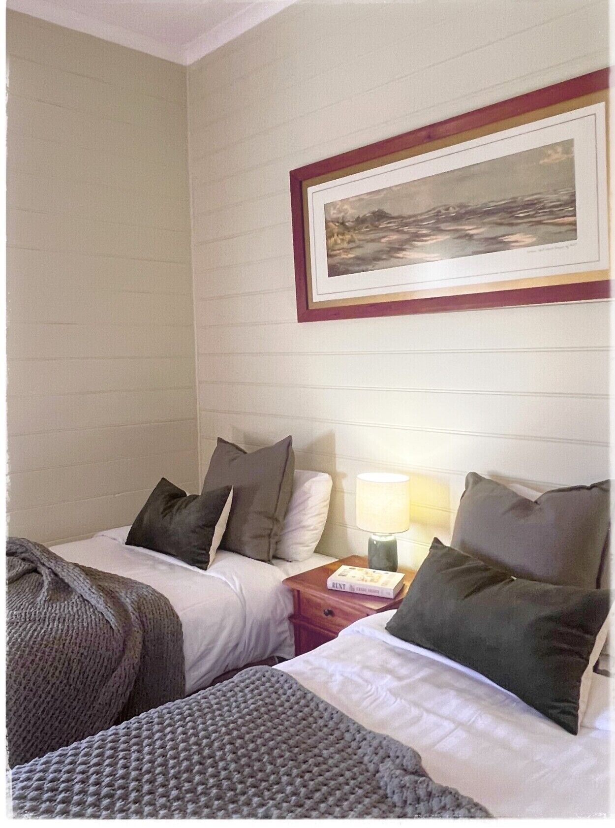 A hotel room with two beds, a nightstand with a lamp, and a framed picture on the wall.