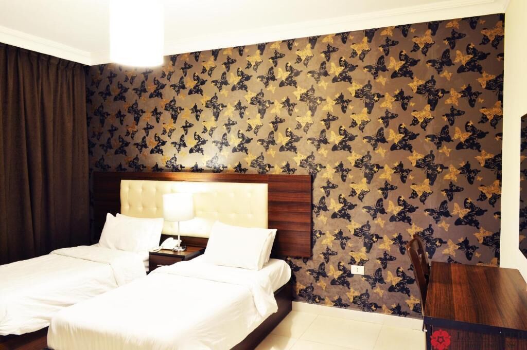 A hotel room with a large bed, a wooden headboard, and a patterned wallpaper.