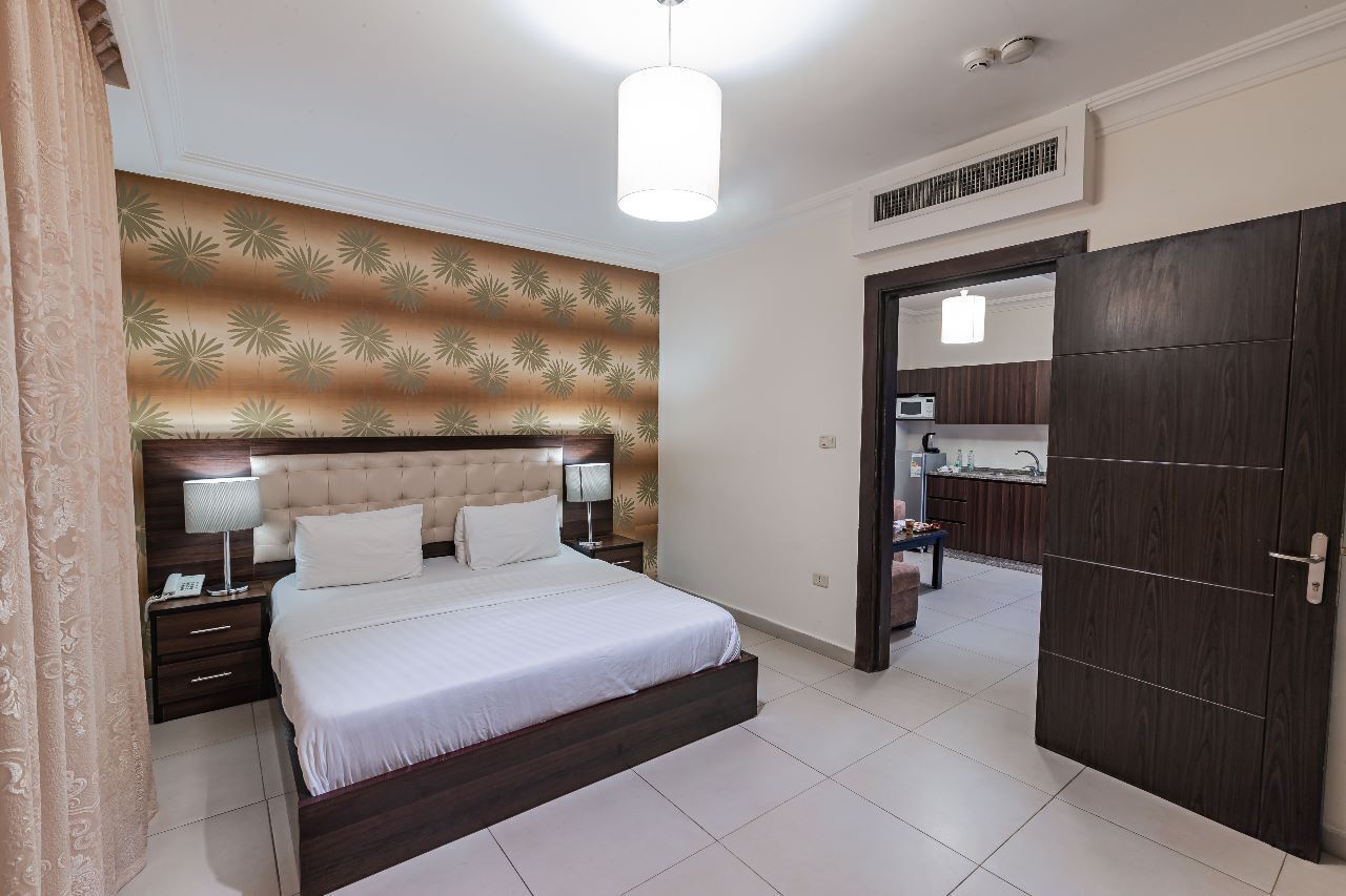 Camera d'albergo con un letto grande, un comodino, una lampada, un armadio e una porta che conduce al bagno.