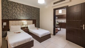 Habitación de hotel con dos camas, un cabecero de madera, una mesita de noche con una lámpara, un teléfono y un baño visible a través de una puerta abierta.