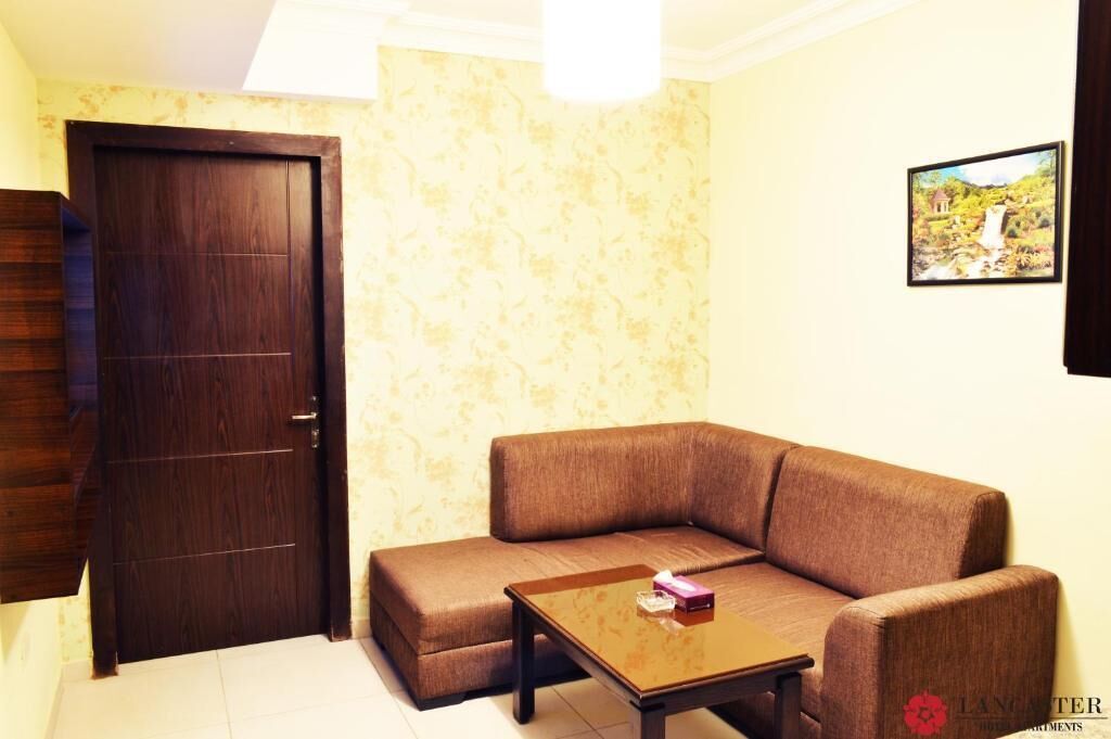 Ein Wohnzimmer mit braunem Sofa, einem Holztisch, einer dunkelbraunen Holztür und einem an der Wand hängenden Bild.