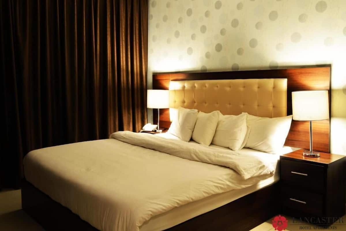 A hotel room with a large bed, two bedside tables with lamps, a wooden headboard, and a polka dot wall.