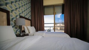 Habitación de hotel con dos camas, una mesita de noche con lámpara y una ventana con cortinas.