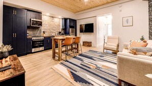 A modern kitchen with dark cabinets, a wooden ceiling, and a dining area with a striped rug. - Parliament Views | Historic Stone Apartment in Old Quebec (Québec)