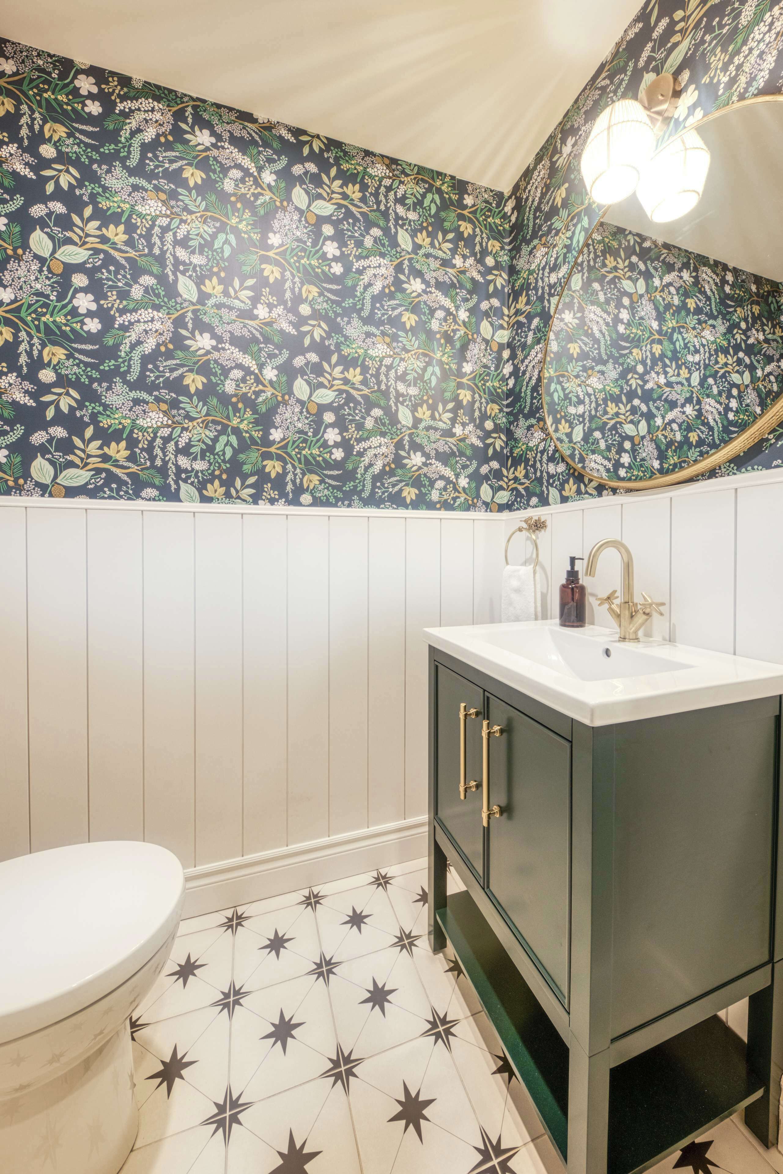 A bathroom with a floral wallpaper, a white toilet, a sink with gold fixtures, and a star-patterned floor.