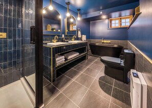 Un baño moderno con pared de azulejos azul oscuro, una bañera independiente, un tocador con detalles dorados y un espejo grande.