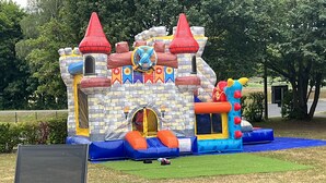 Un castillo inflable con diseño de castillo, que incluye un foso, toboganes y una entrada tipo túnel.