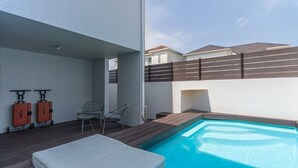 A rooftop pool area with a wooden deck, lounge chairs, and two orange storage units. - Grandioso Okinawa Pool Villa Onna 8 (Onna)