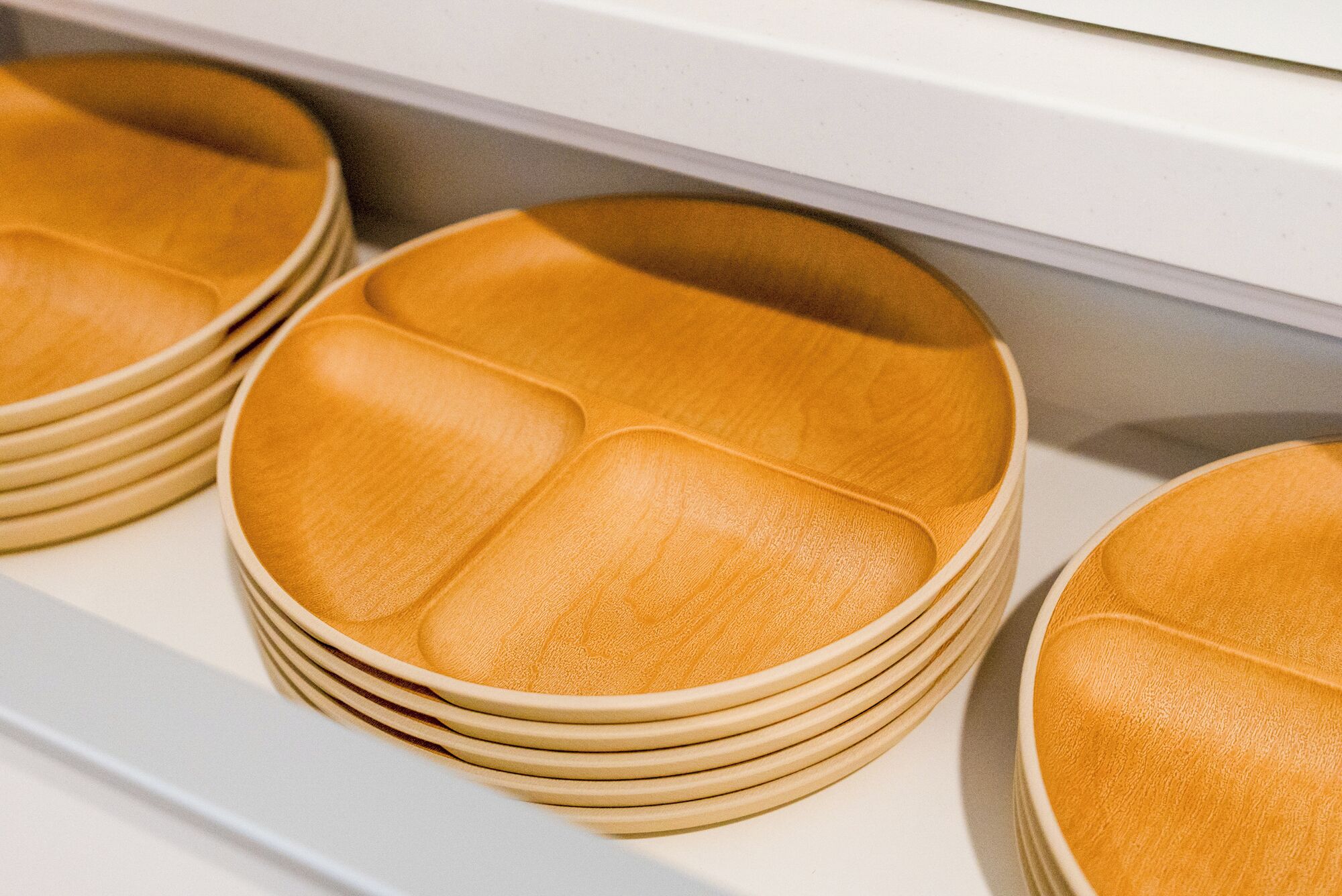 A stack of beige plates with a textured surface, arranged on a shelf.
