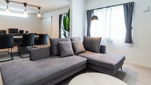 A modern living room with a grey sectional sofa, a round coffee table, and a dining area with a table and chairs. - Grandioso Okinawa Pool Villa Onna 8 (Onna)