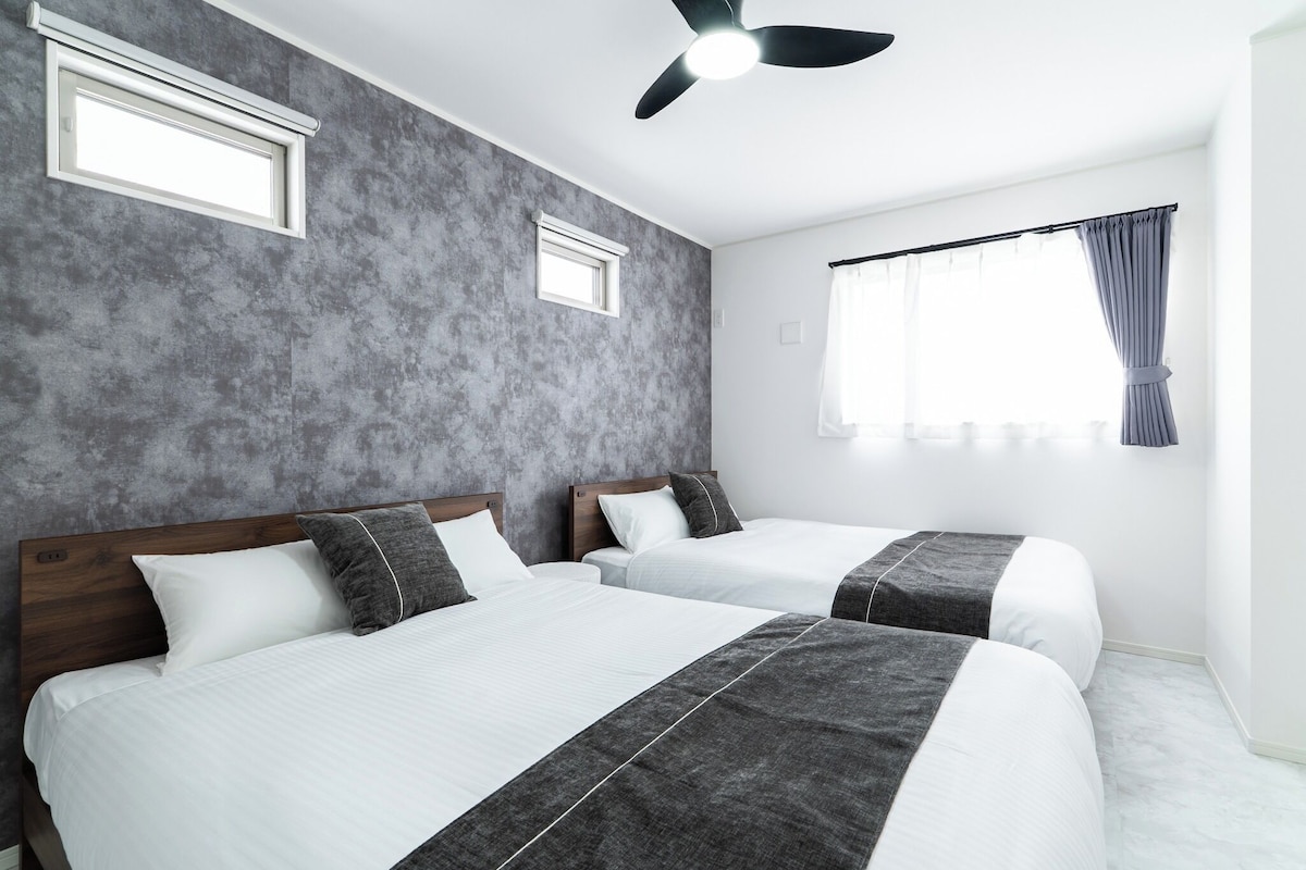 A hotel room with two beds, a ceiling fan, and a window with curtains.