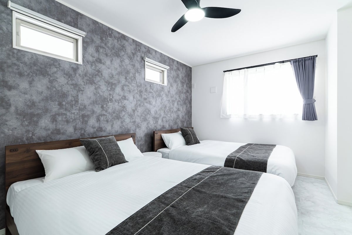 Habitación de hotel con dos camas, ventilador de techo, ventana con cortinas y pared texturizada.