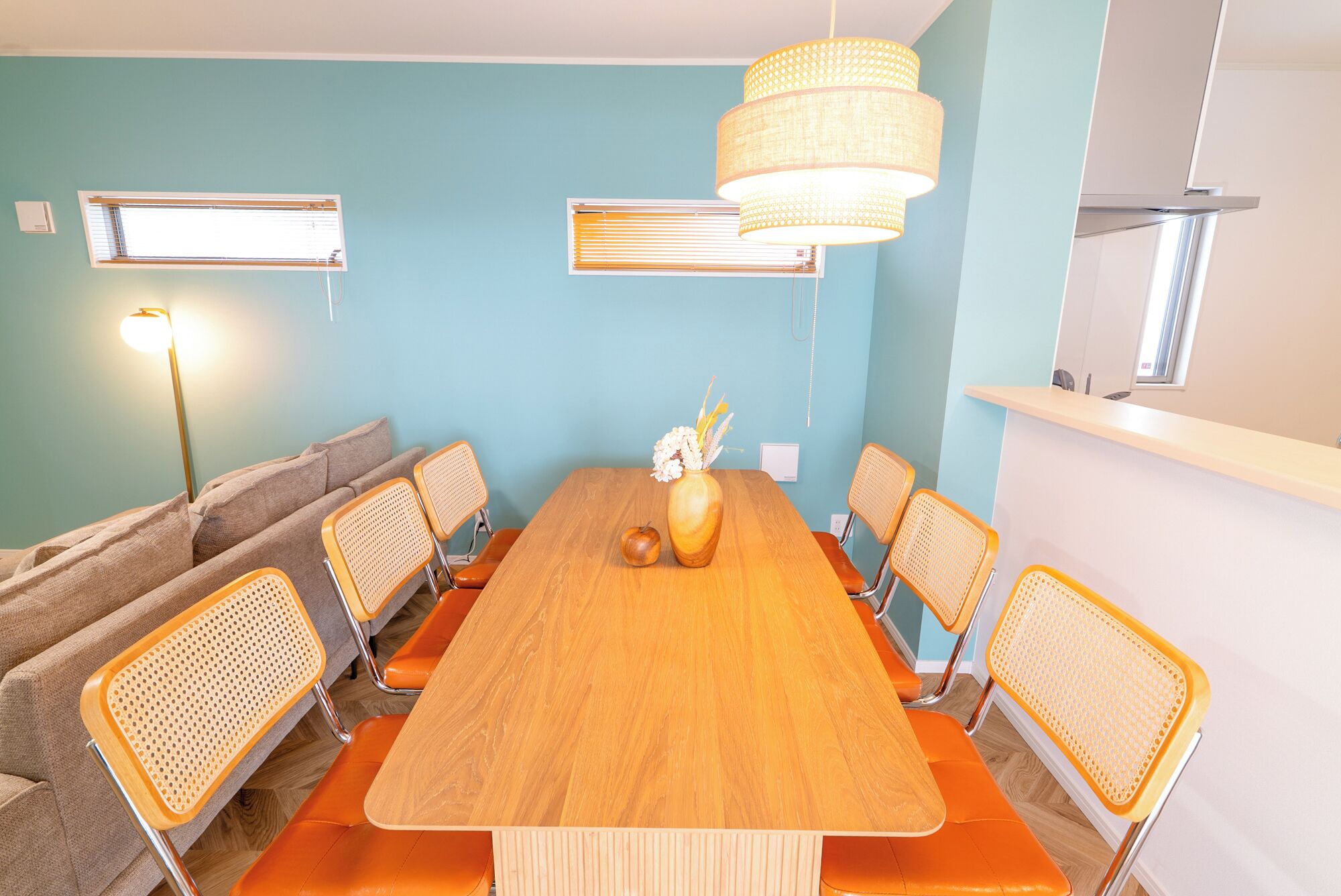 Una sala conferenze con un lungo tavolo di legno, sedie arancioni, un vaso con fiori e una lampada a sospensione.