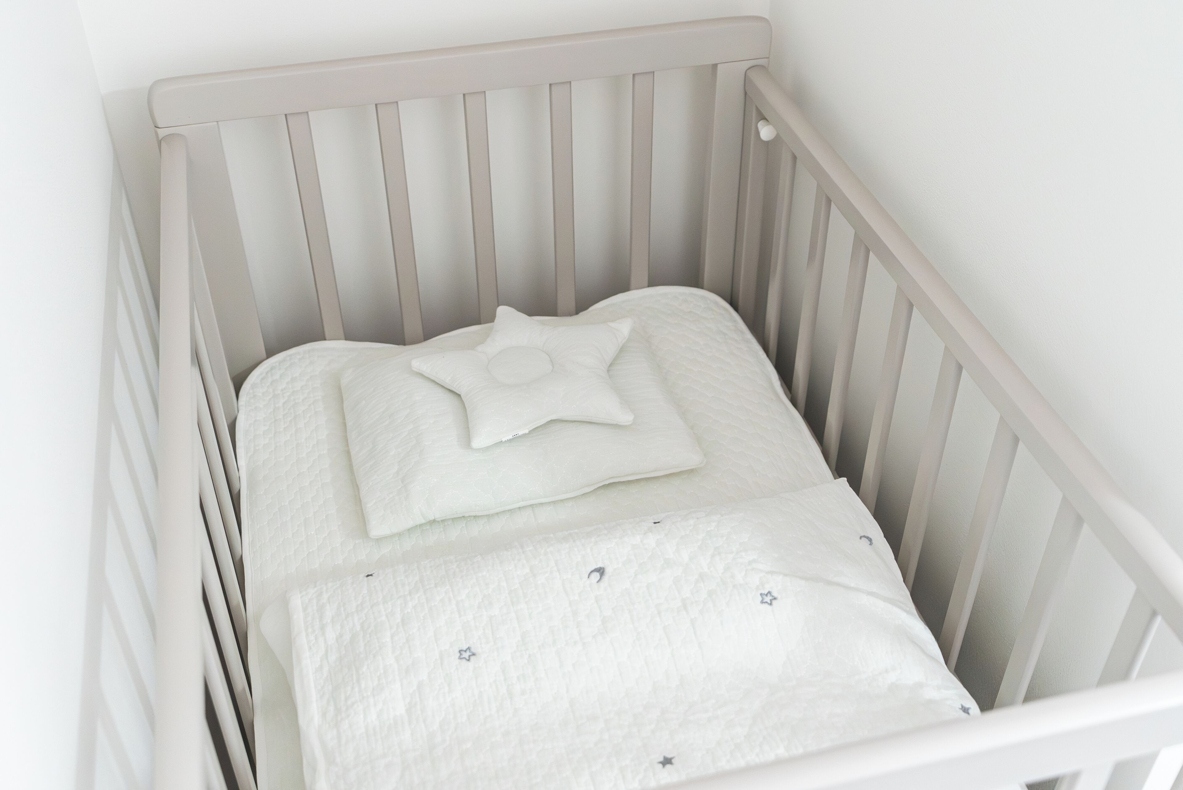 Ein weißes Babybett mit einem sternförmigen Kopfkissen und einer gesteppten Decke.