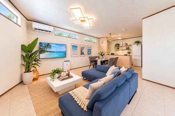 A modern living room with a blue sofa, a coffee table, and a TV displaying a scenic view of Okinawa. - Grandioso Okinawa Pool Villa Onna 8 (Onna)