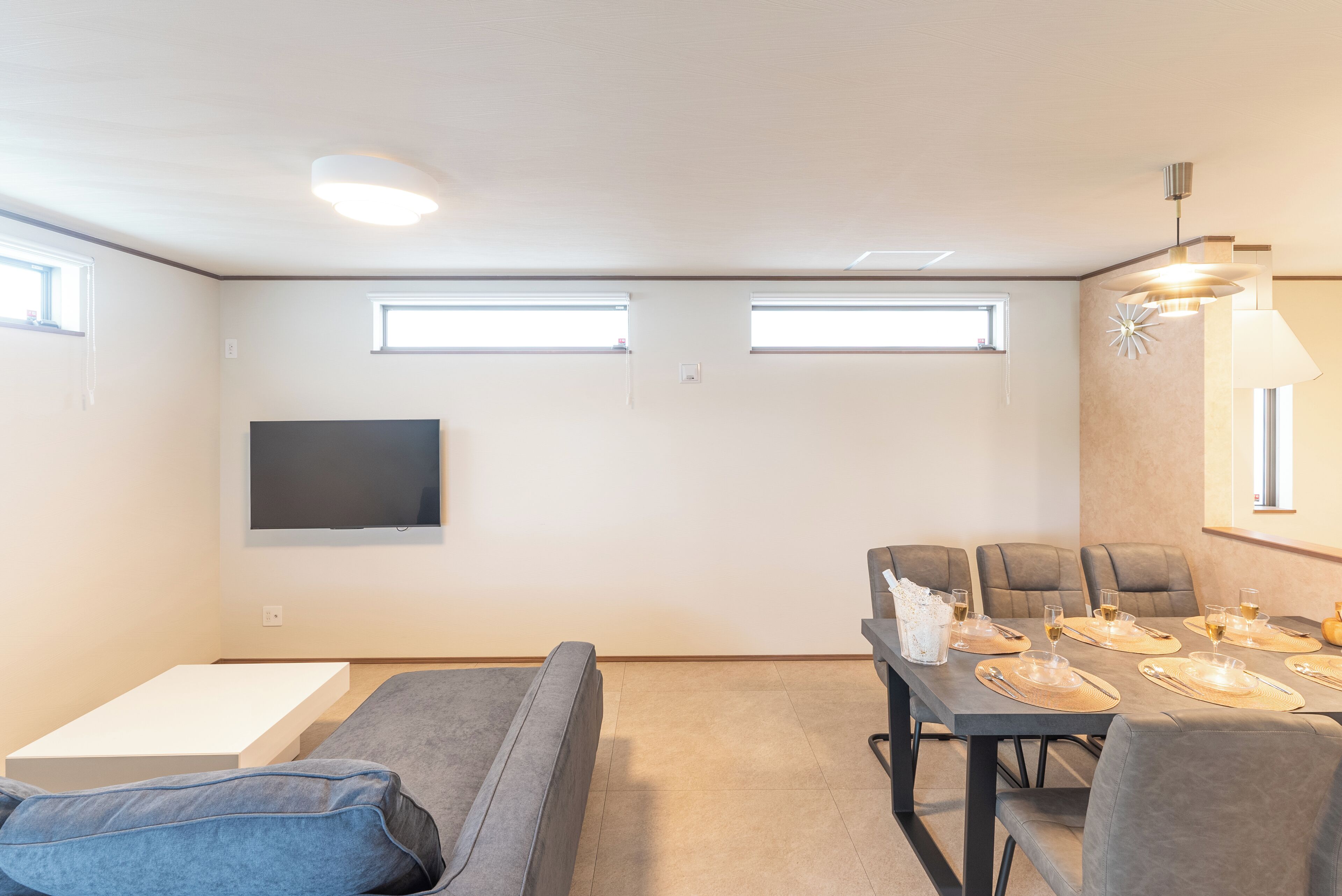 A modern living room with a sofa, a dining table set for four, and a flat-screen TV mounted on the wall.