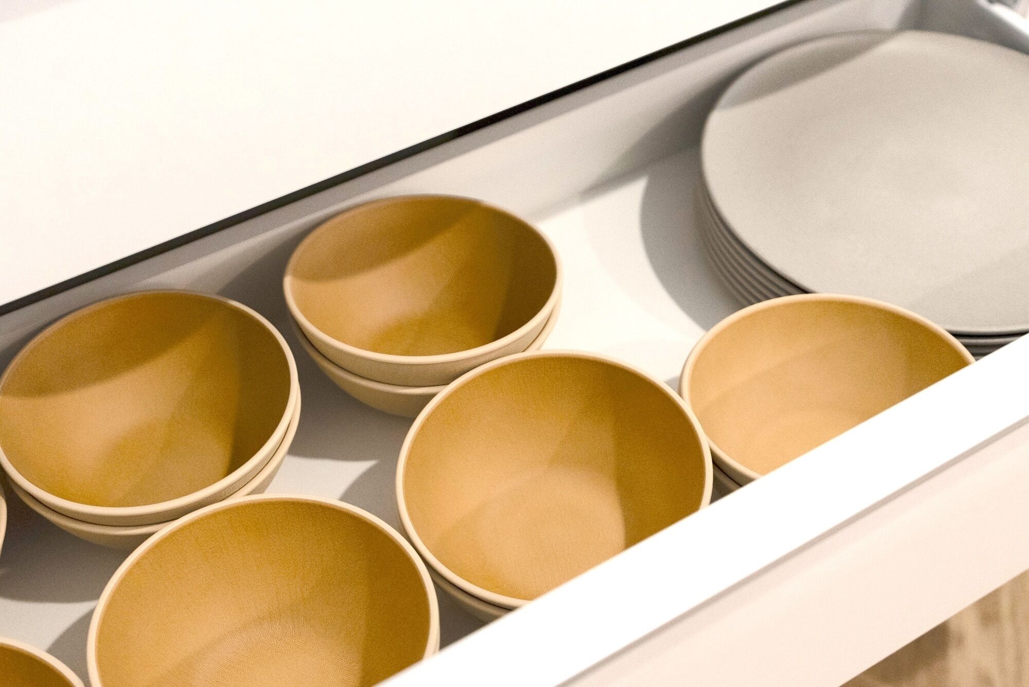 A drawer containing several beige bowls and a stack of white plates.