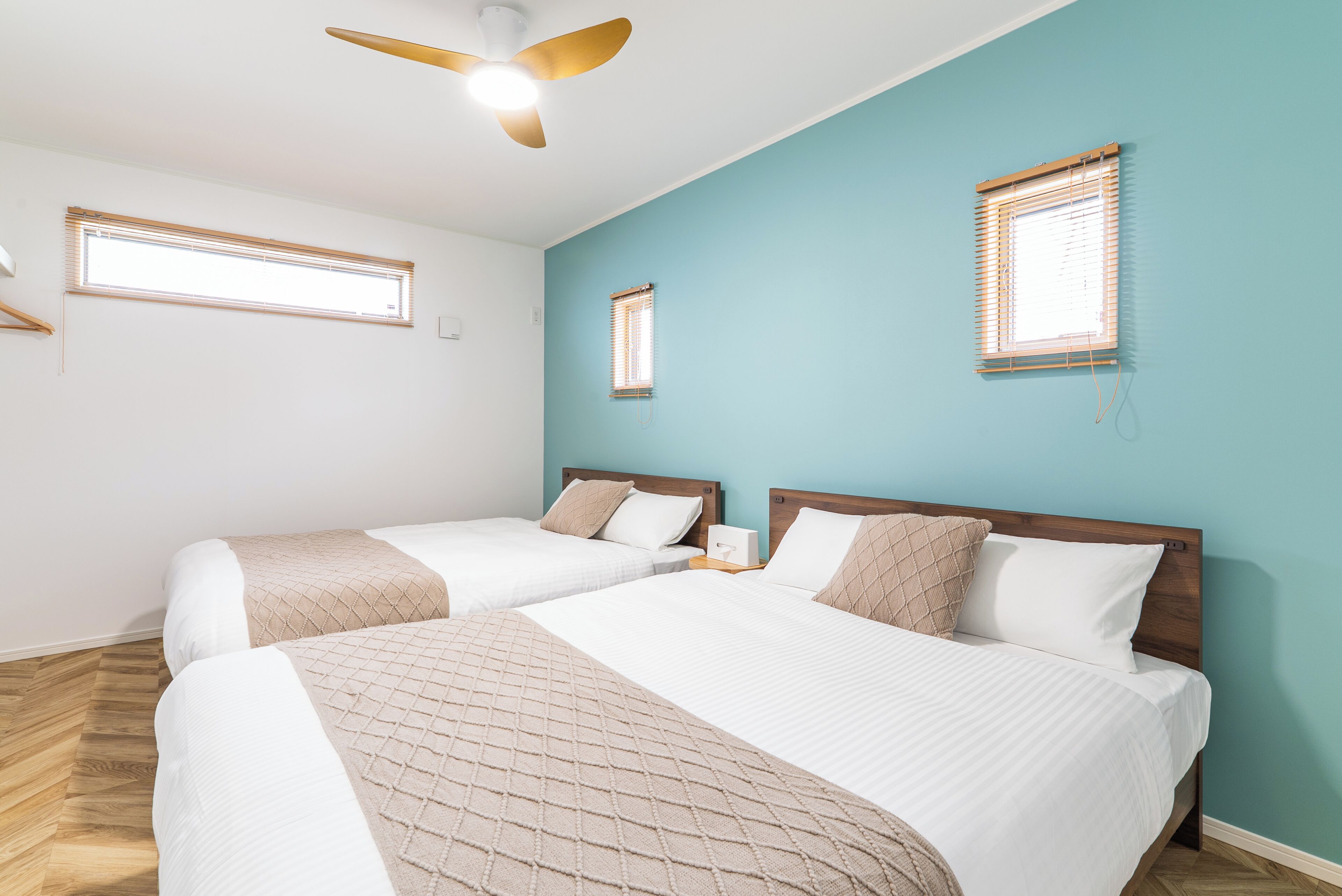 A bedroom with two beds, a ceiling fan, and two windows with blinds.