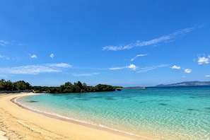 A beach with clear turquoise water, a sandy shore, and a distant island with vegetation. - Grandioso Okinawa Pool Villa Onna 8 (Onna)