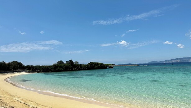 A beach with clear turquoise water, a sandy shore, and a distant view of land with vegetation and a boat. - Grandioso Okinawa Pool Villa Onna 8 (Onna)