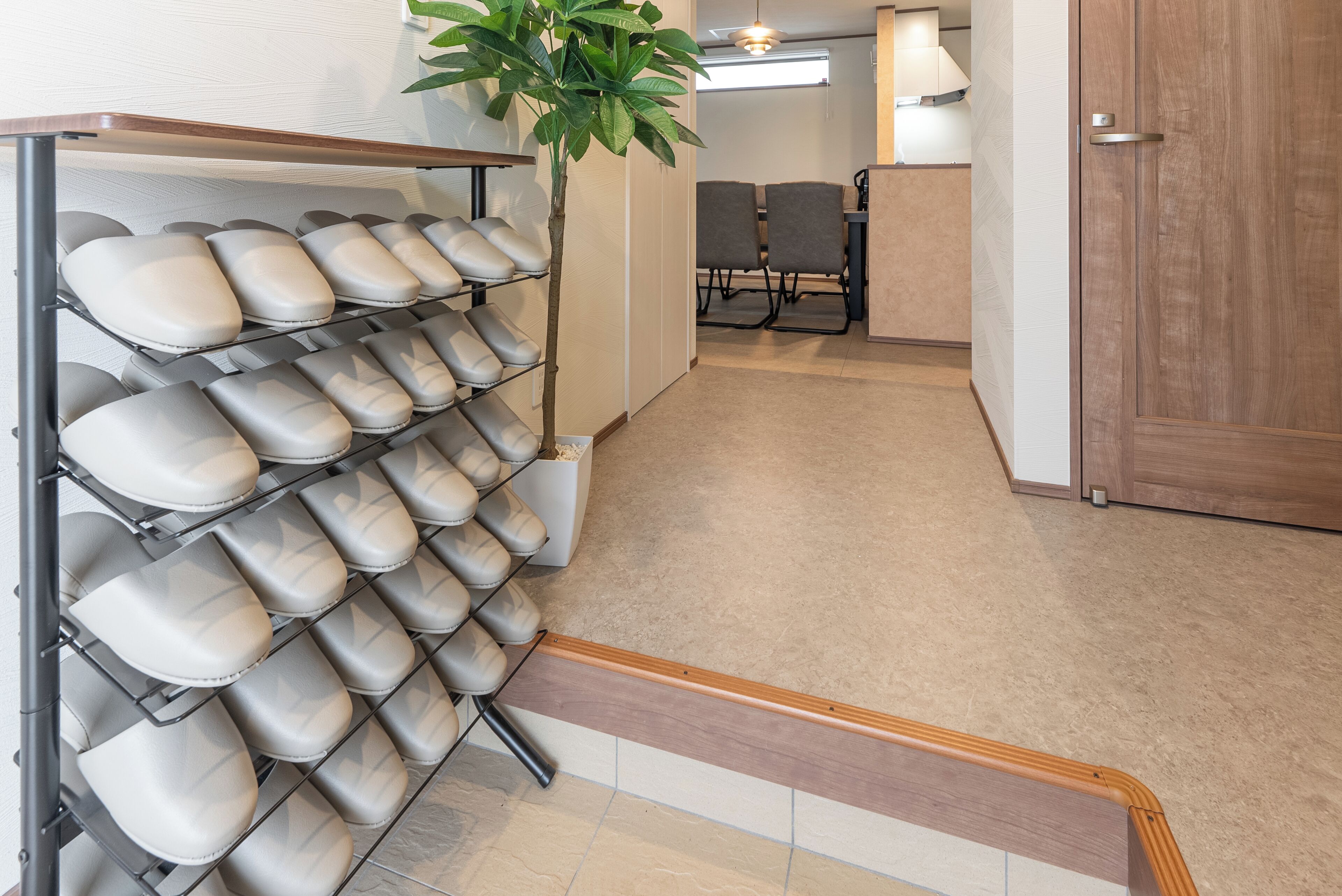 A shoe rack with multiple pairs of shoes, a wooden handrail, and a potted plant in a hallway.