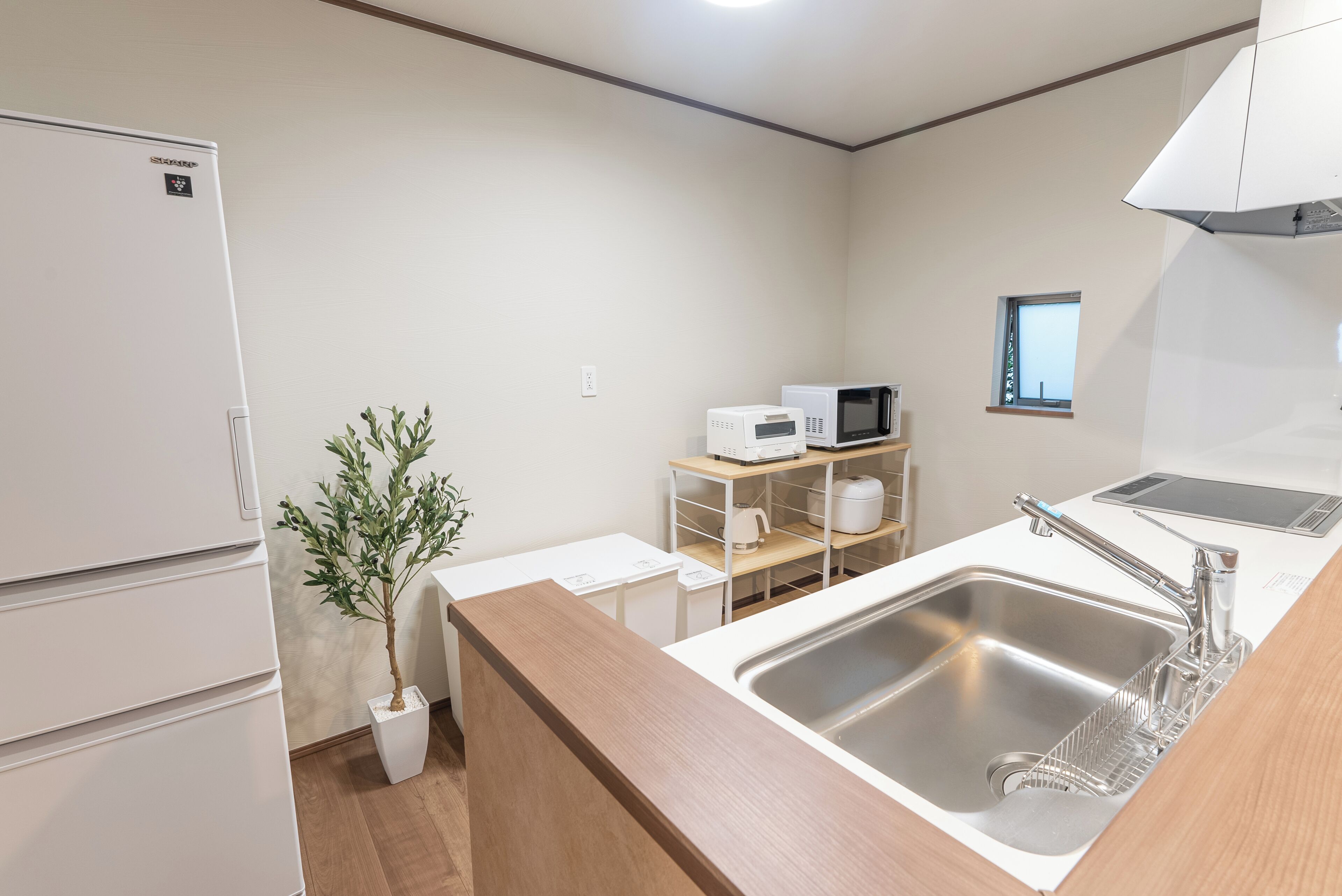 A compact kitchen with a refrigerator, microwave, sink, and a small window.