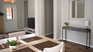 Ett modernt vardagsrum med en matplats, en tv, ett avlastningsbord med en växt och en spegel på väggen.