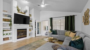 Una sala de estar con chimenea, un sofá gris, una mesa de centro y un televisor.