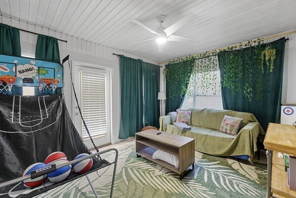 Una habitación con aro de baloncesto, un sofá, una mesita y una ventana con cortinas.