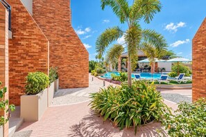 A pool area with lounge chairs, a palm tree, and a brick building.